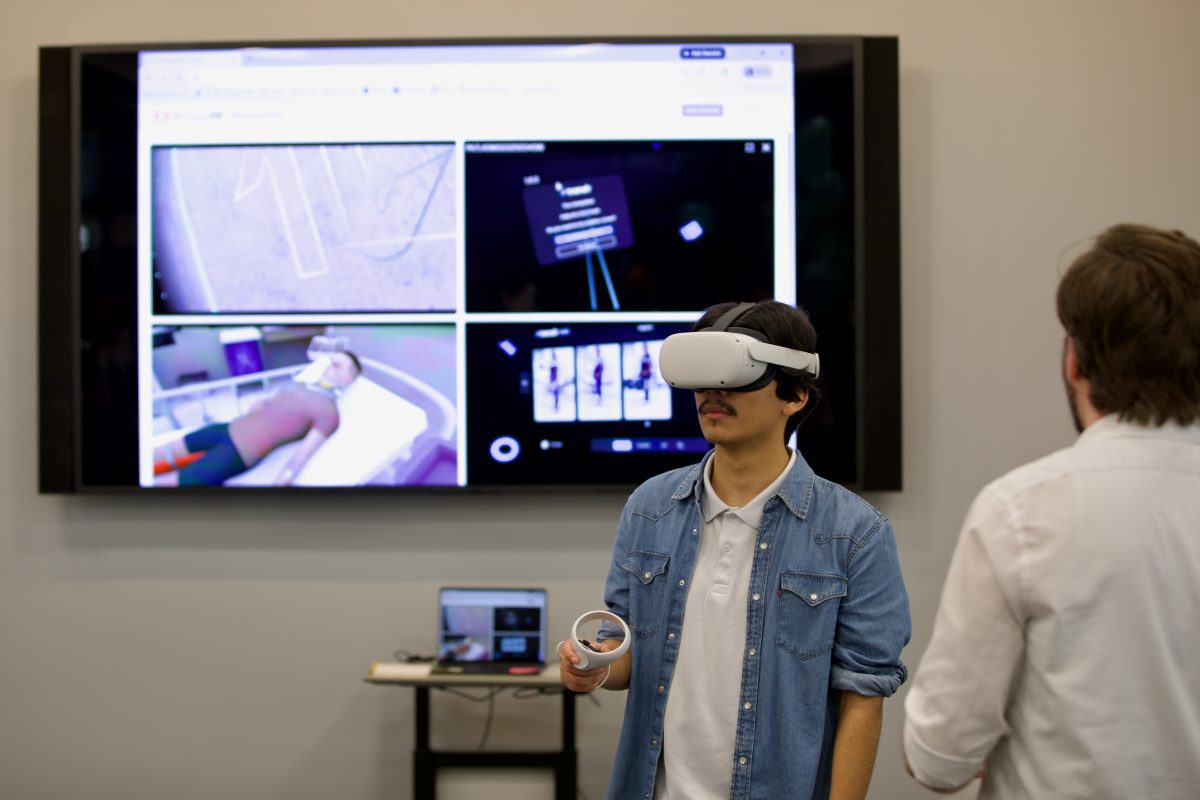 Student using virtual reality headset and controller with screen in background showing what the student is seeing.